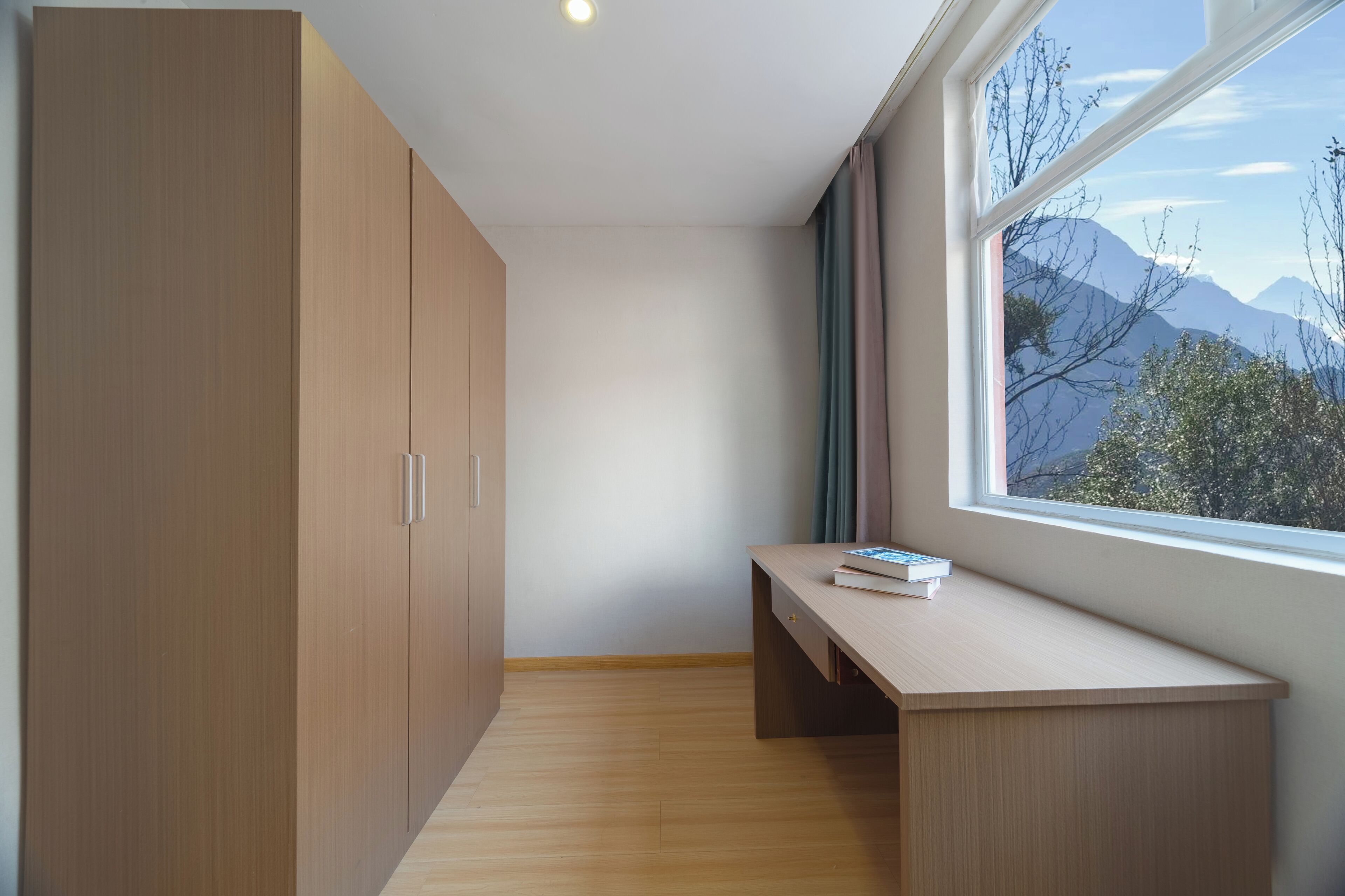 Una habitación con escritorio, ventana con vistas a la montaña y armarios de madera.