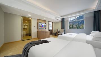 A hotel room with two beds, a TV, a desk, and a window with a mountain view.