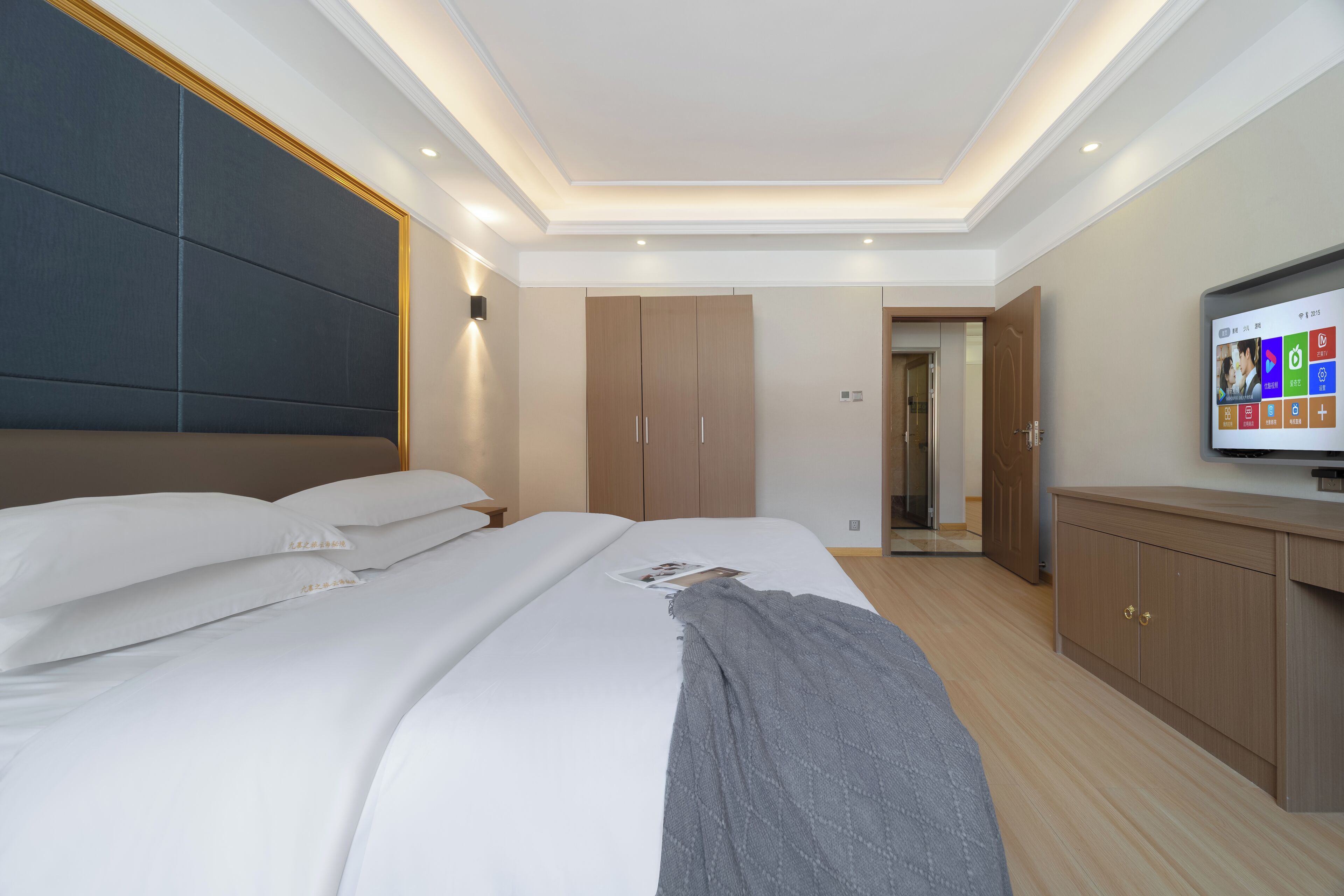 A modern bedroom with a large bed, a TV, and a wardrobe.