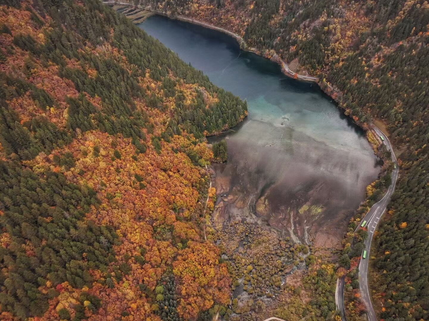 Une vue aérienne d’un lac entouré de collines boisées, avec une route sinueuse.