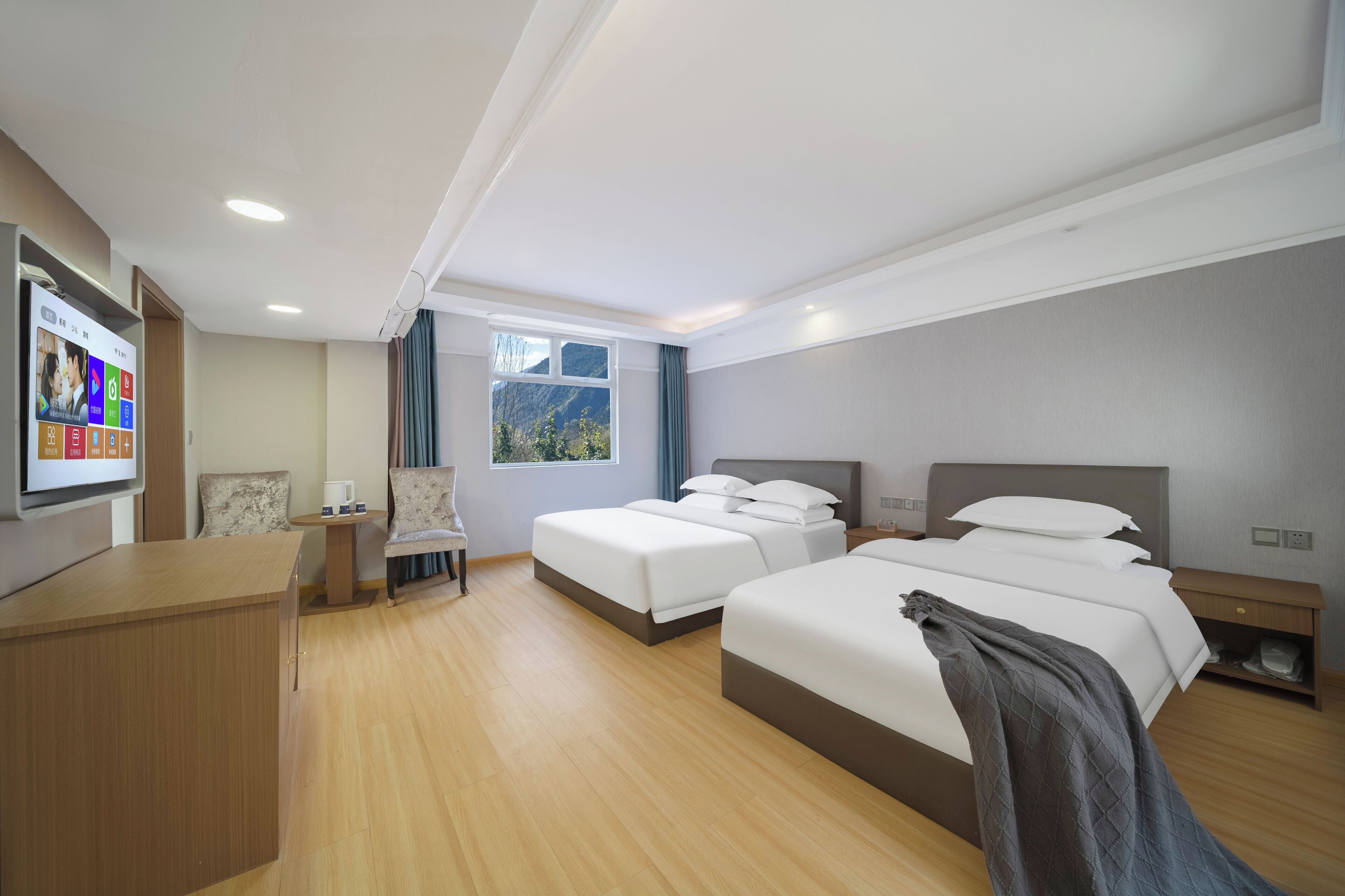 A hotel room with two beds, a desk, a chair, a TV, and a window with a mountain view.
