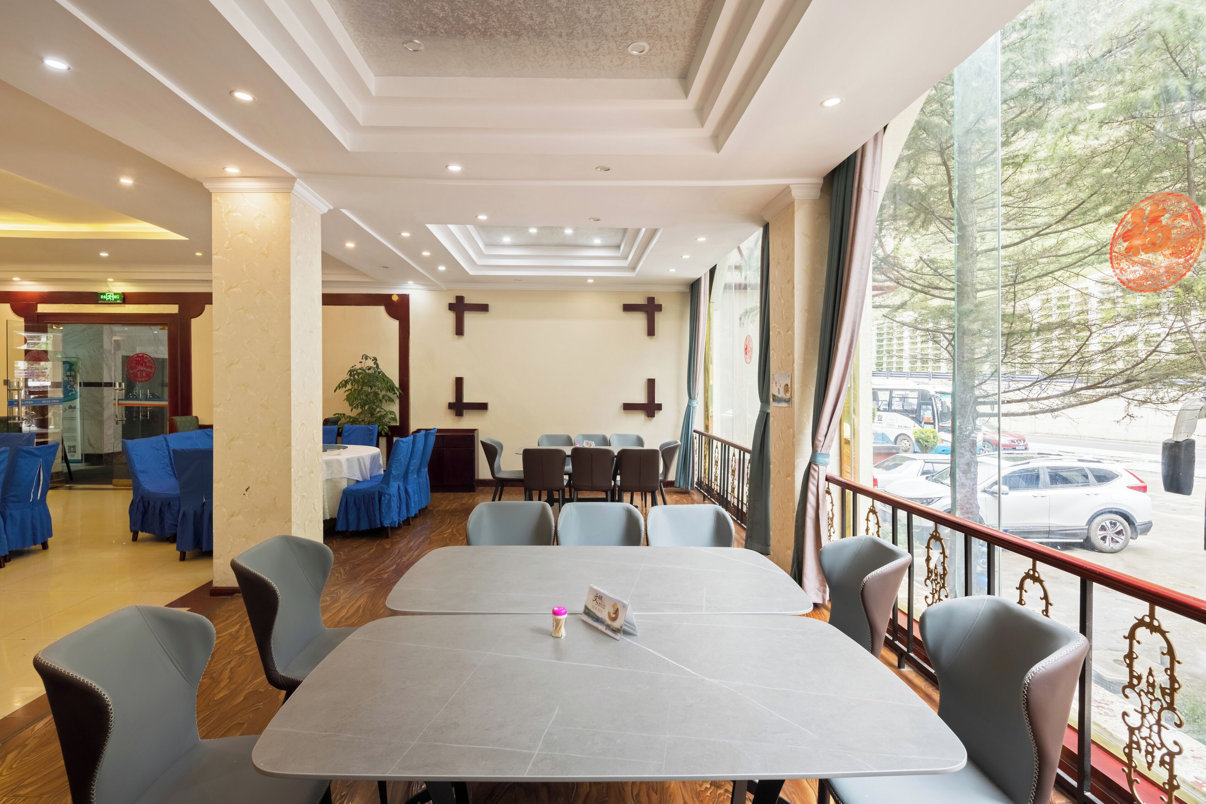 A restaurant with a large table and chairs, a view of the street, and a ceiling with recessed lighting.