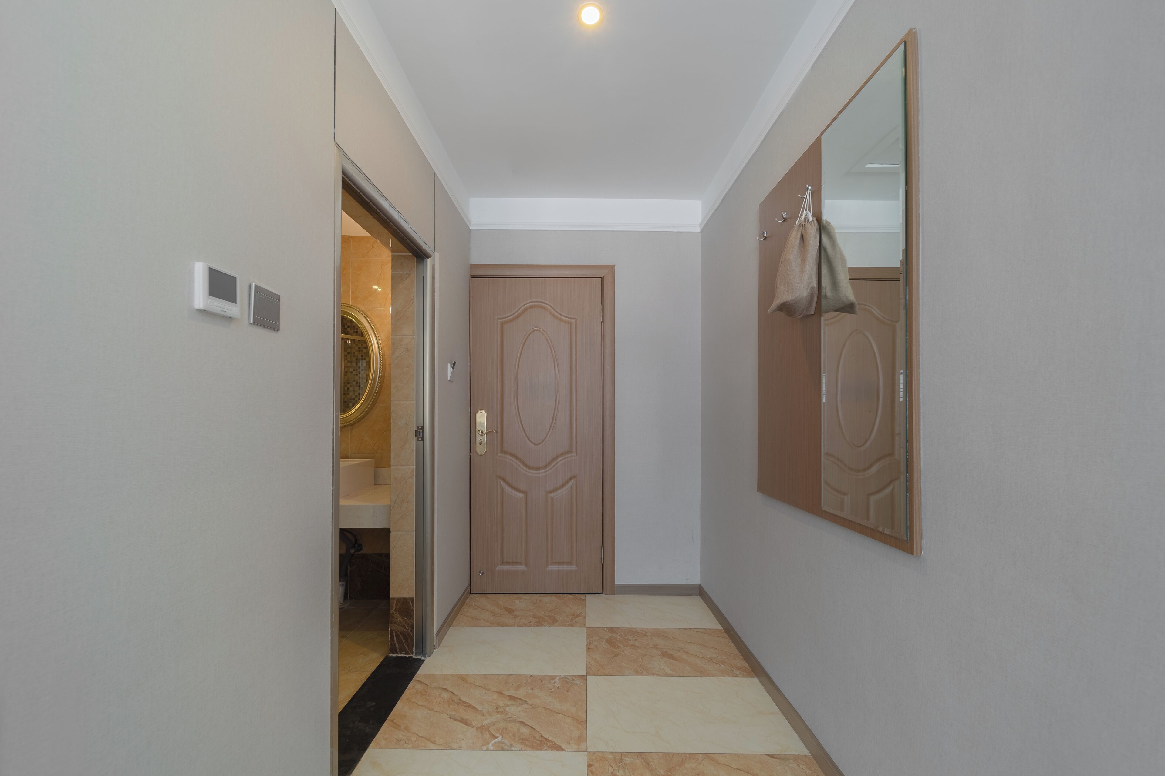Um corredor com piso xadrez, uma porta com espelho e um candeeiro no teto.