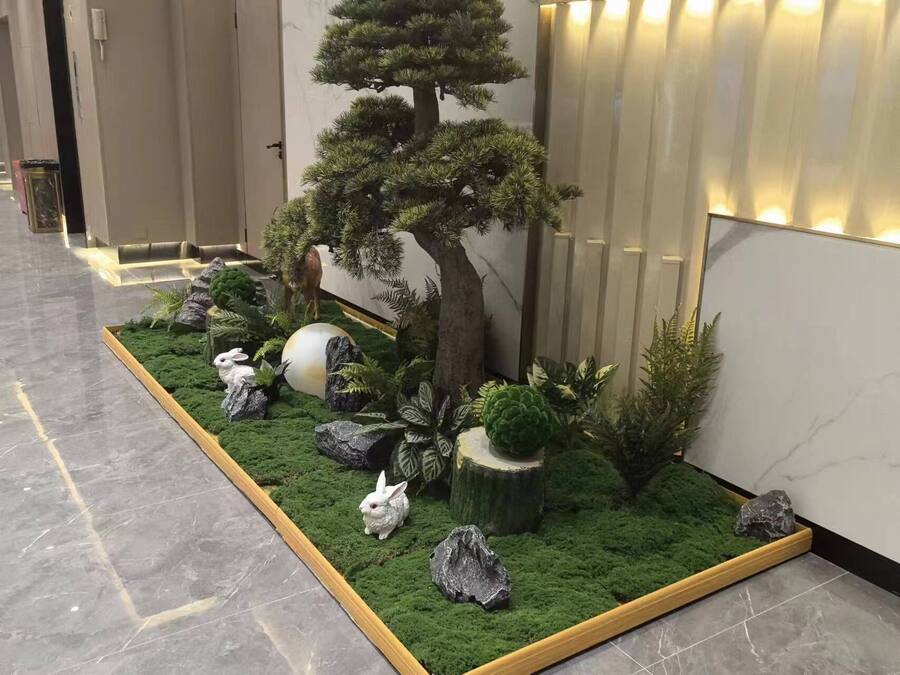 A small indoor garden with a bonsai tree, rocks, and a white rabbit figurine.