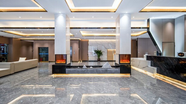 A modern lobby with a marble floor, a reception desk, a sofa, and a staircase.