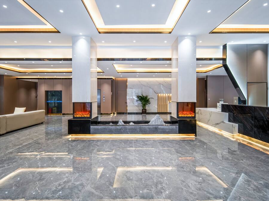 A modern lobby with a marble floor, a reception desk, a sofa, and a staircase.