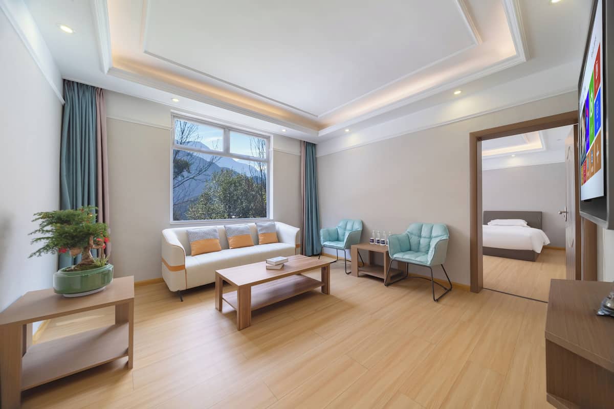 Ein modernes Hotelzimmer mit einer Couch, einem Holztisch, zwei Sesseln, einem kleinen Beistelltisch, einem Bett und einem Fernseher.