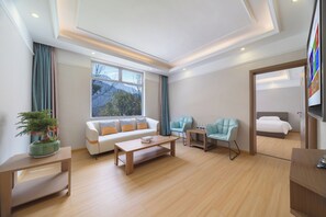 Une chambre d’hôtel moderne comprenant un canapé, une table basse en bois, deux fauteuils, une petite table d’appoint, un lit et un téléviseur.