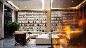 A modern lobby with a large bookshelf, comfortable seating, and a large plant.