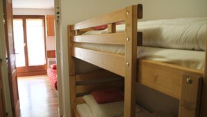 A bunk bed room with a wooden headboard, a red pillow, and a white pillow. - Gentianes Gna17 Cosy & Mountain 4 Pers (Chatel)