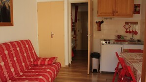 A compact living space with a red-striped sofa, a small kitchen with wooden cabinets, and a dining area with red chairs. - Gentianes Gna17 Cosy & Mountain 4 Pers (Chatel)