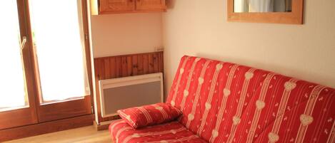 Un sofá rojo con motivos de corazones, un mueble de madera y un radiador.