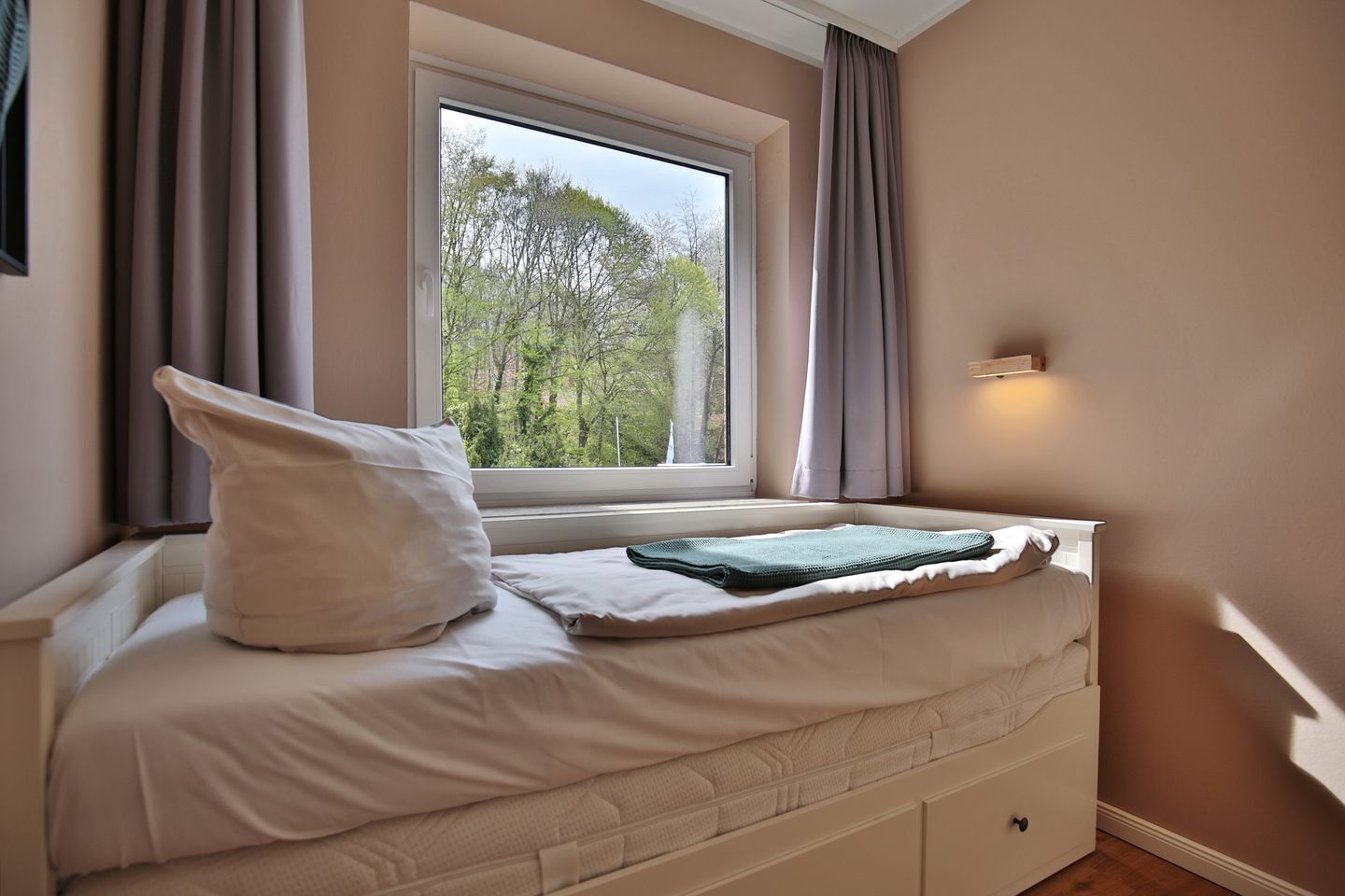 Ein Schlafzimmer mit Fenster, einem Bett, einem Nachttisch und einem Beistelltisch.