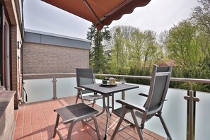 Un balcon extérieur avec une table et des chaises, un mur en briques et une vue sur les arbres.