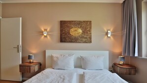 Une chambre d’hôtel avec un grand lit, deux tables de chevet, une œuvre d’art accrochée au mur et deux appliques murales.