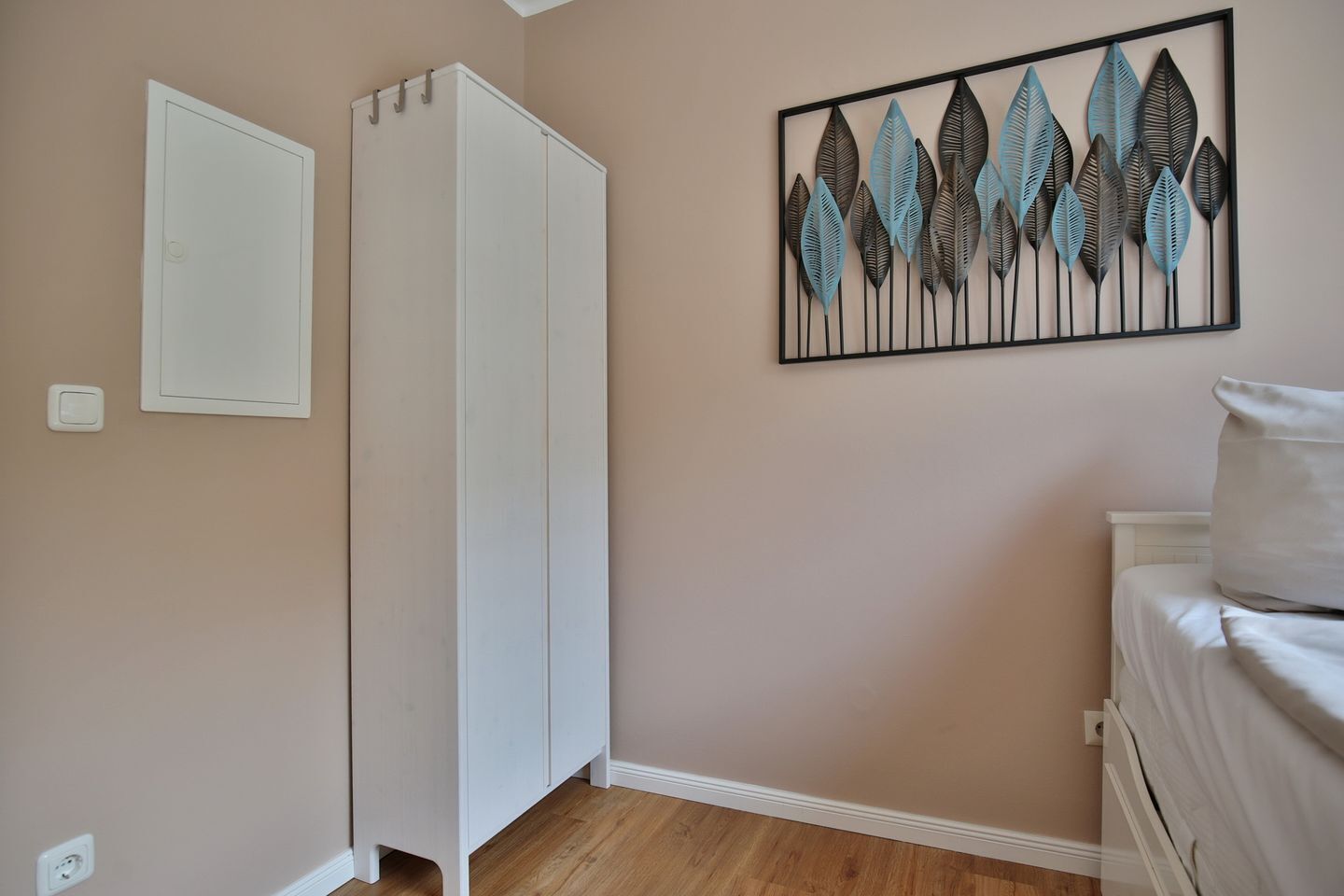 A bedroom with a wardrobe, a bed, and a wall-mounted artwork.