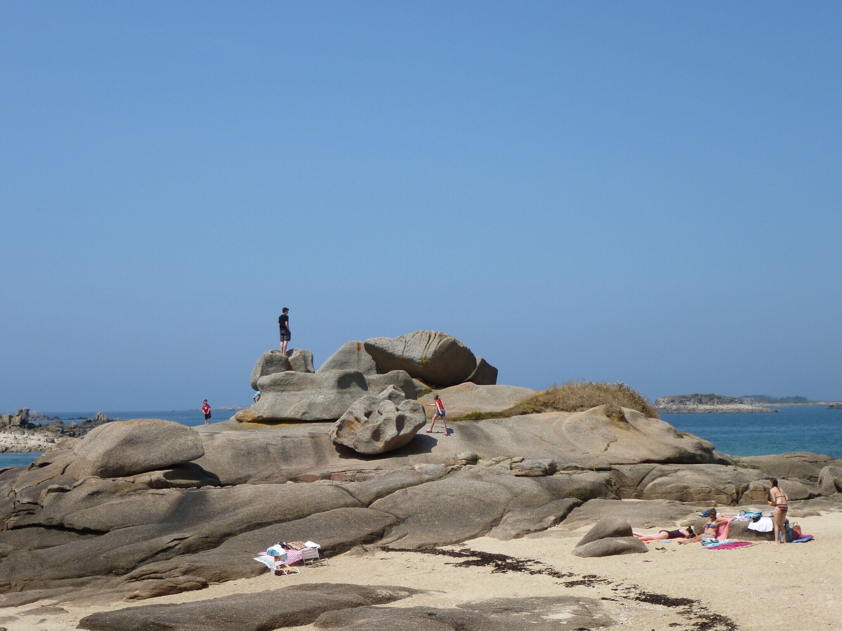 Una playa rocosa con grandes rocas, algunas personas y cielo despejado.