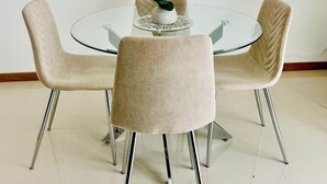 Un tavolo rotondo in vetro con quattro sedie beige rivestite, un vaso con un'orchidea bianca e uno specchio grande appeso sopra.