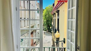 Un ingresso che si affaccia su una strada acciottolata, edifici con balconi e una pianta in vaso sulla destra.