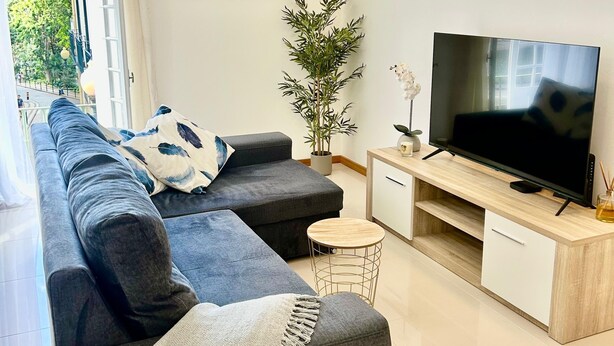 Un soggiorno moderno con un divano angolare grigio, un tavolino rotondo, una TV a schermo piatto su un supporto in legno e una pianta in vaso.