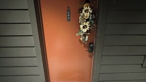 A brown door with a number plate, a welcome mat, and a floral decoration.
