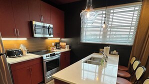 A modern kitchen with stainless steel appliances, a central island with seating, and a window with blinds.
