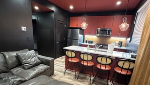 A modern kitchen with a central island, dark walls, and a leather sofa in a living area.