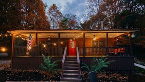 A wooden cabin with a porch, a red door, and a staircase leading to the entrance. - Log Haus- Cabin in Amish Country (Danville)