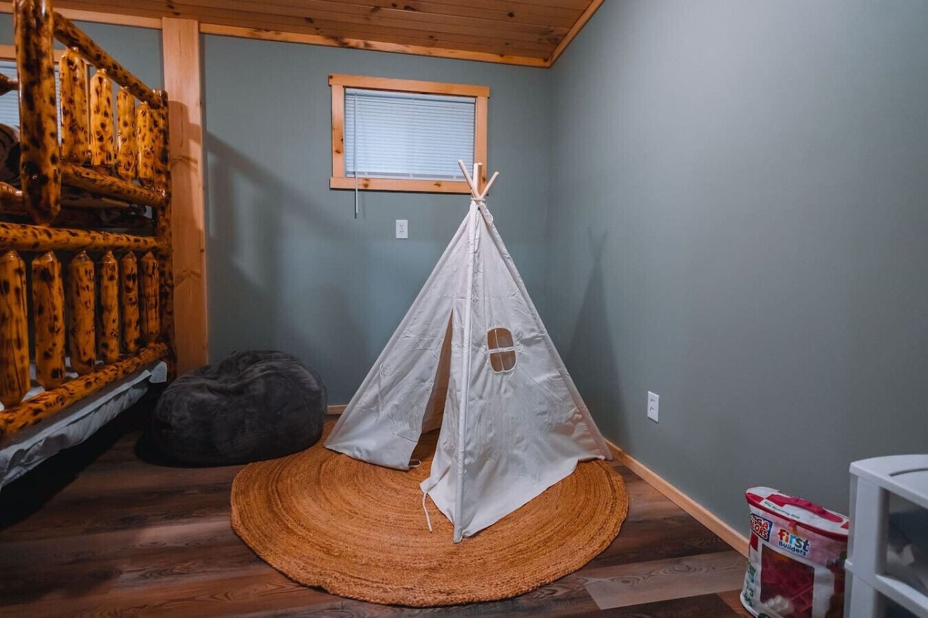 Una habitación con una escalera de madera, un tipi blanco, un sillón de cuero negro y un tapiz tejido.