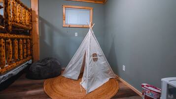 Una habitación con una escalera de madera, un tipi blanco, un sillón de cuero negro y un tapiz tejido.