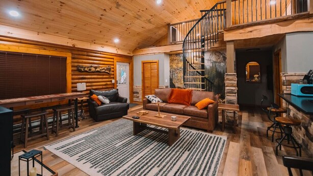 A log cabin interior with a dining area, two sofas, a coffee table, and a staircase. - Log Haus- Cabin in Amish Country (Danville)