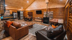 A log cabin interior with a dining area, a fireplace, a TV, and a kitchen with a refrigerator. - Log Haus- Cabin in Amish Country (Danville)