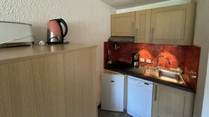 A compact kitchen with wooden cabinets, a white dishwasher, a coffee maker, and a red-tiled backsplash. - Hameau DES 4 Saisons Hsc113 Mountain & View 6 Pers (Chatel)