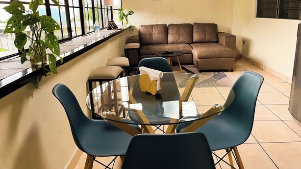 Ein modernes Wohnzimmer mit Glastisch, blauen Stühlen, einem braunen Sofa und einem Stadtbild an der Wand.