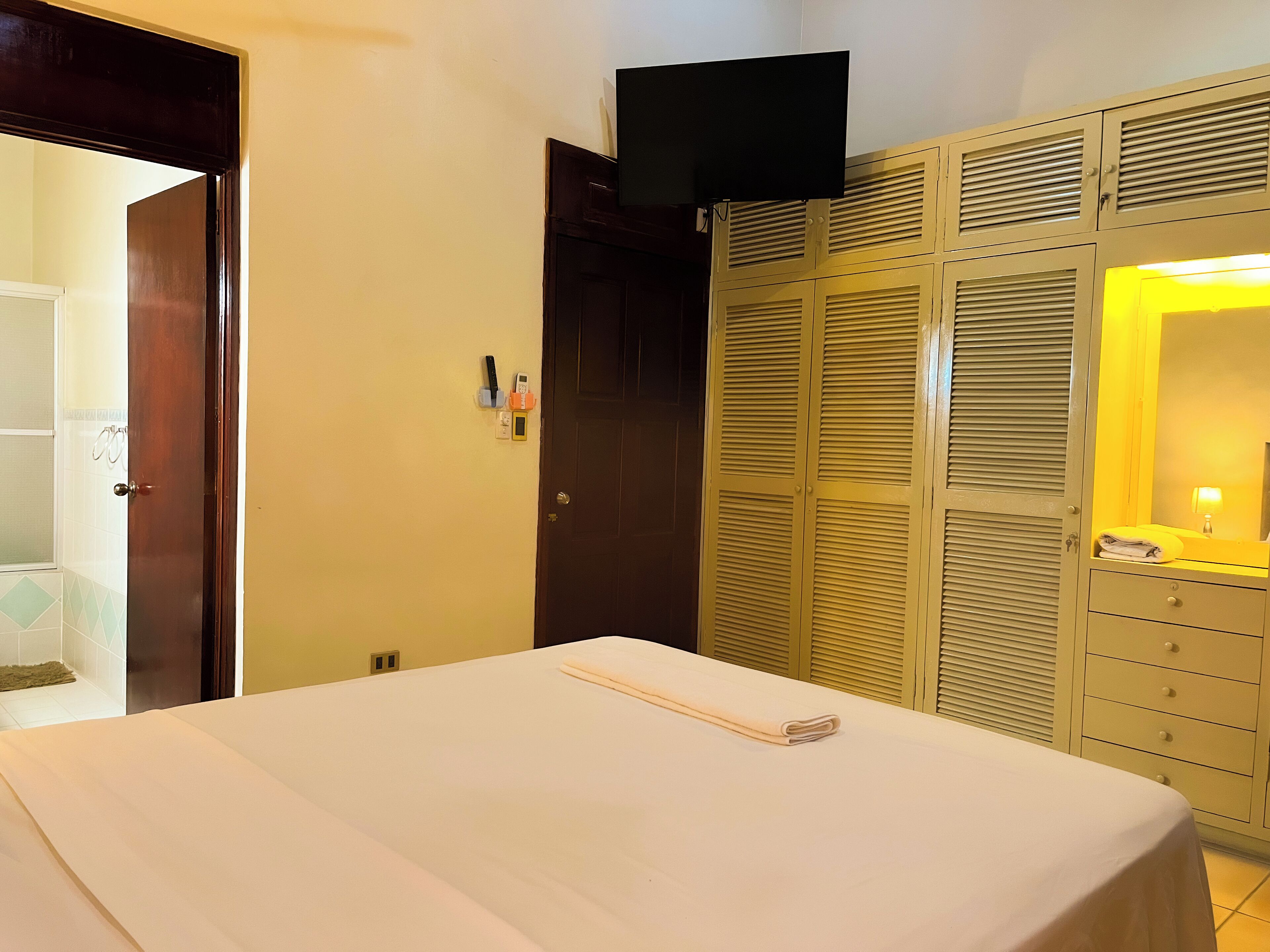 A hotel room with a bed, a wardrobe with a mirror, and a television mounted above the wardrobe.