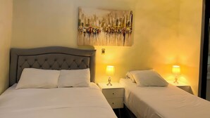 Ein Hotelzimmer mit zwei Einzelbetten, jeweils mit einem Nachttisch und einer Lampe. Darüber hängt ein großes, abstraktes Gemälde an der Wand.