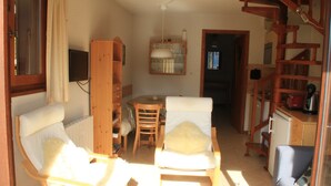 A cozy living room with two white armchairs, a wooden sideboard, a small table, and a kitchen area visible through an open doorway. - Barbessine Bbb11 SUN & Chair Lift 5 Pers (Chatel)