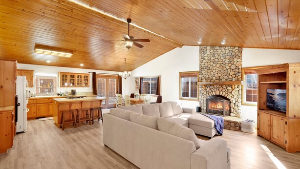 Un salón espacioso con un sofá grande, techo de madera, chimenea de piedra y armarios de madera.