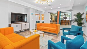 Ein modernes Wohnzimmer mit großem Flachbildfernseher, orange- und blauer Einrichtung und einer Deckenleuchte.