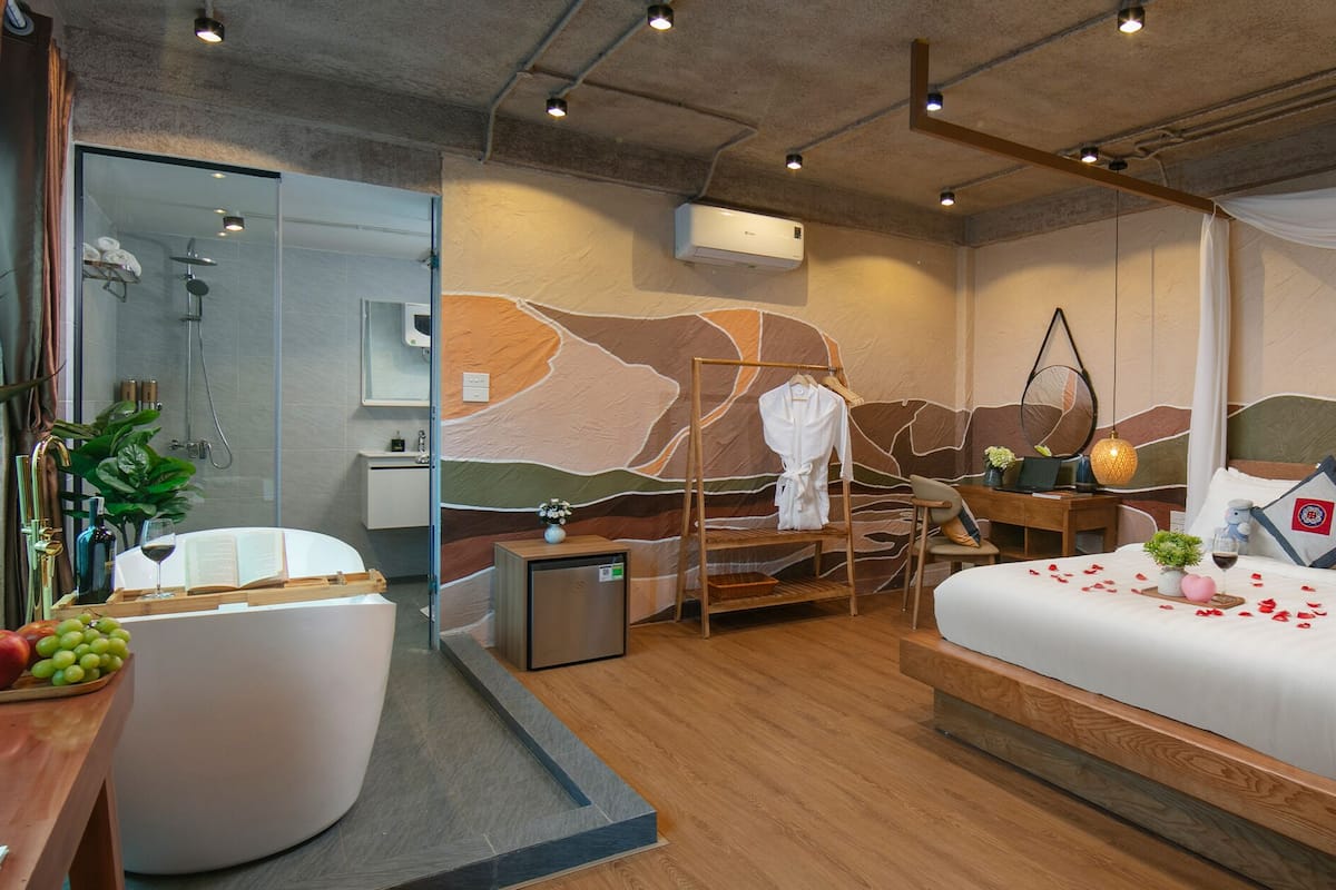 A modern hotel room with a large bed, a desk, a shower area, and a small seating area.
