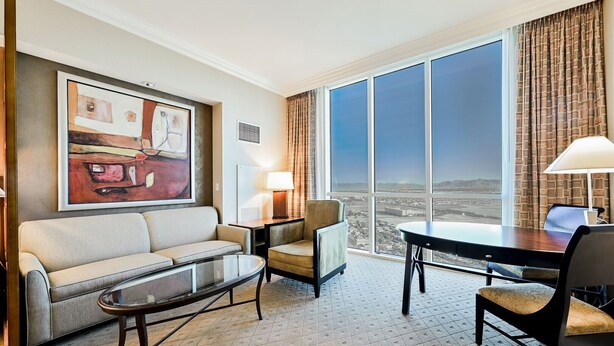 A hotel room with a large window, a sofa, a chair, a small table, and a lamp. - SVS: Penthouse 2BD/3BA | Mountain View Balcony | Full Kitchen | MGM (Las Vegas)