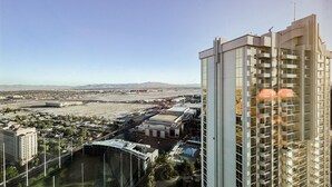 A high-rise building with multiple balconies, a parking area, and a view of a distant airport and mountains. - SVS: Penthouse 2BD/3BA | Mountain View Balcony | Full Kitchen | MGM (Las Vegas)