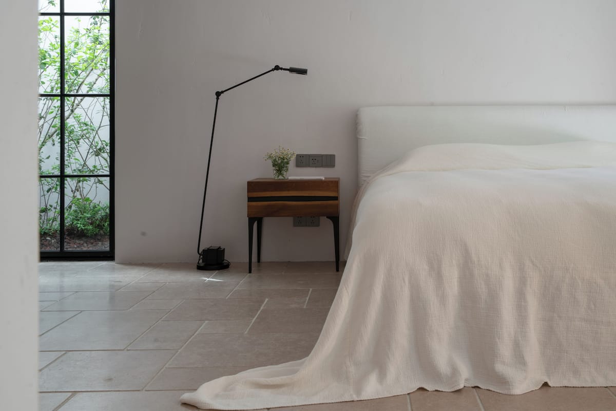 Une chambre à coucher comprenant un lit, une table de chevet, une lampe sur pied et une fenêtre donnant sur un paysage verdoyant.