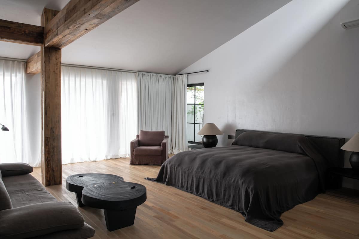 Une chambre moderne avec un grand lit, un fauteuil marron et une table ronde noire.