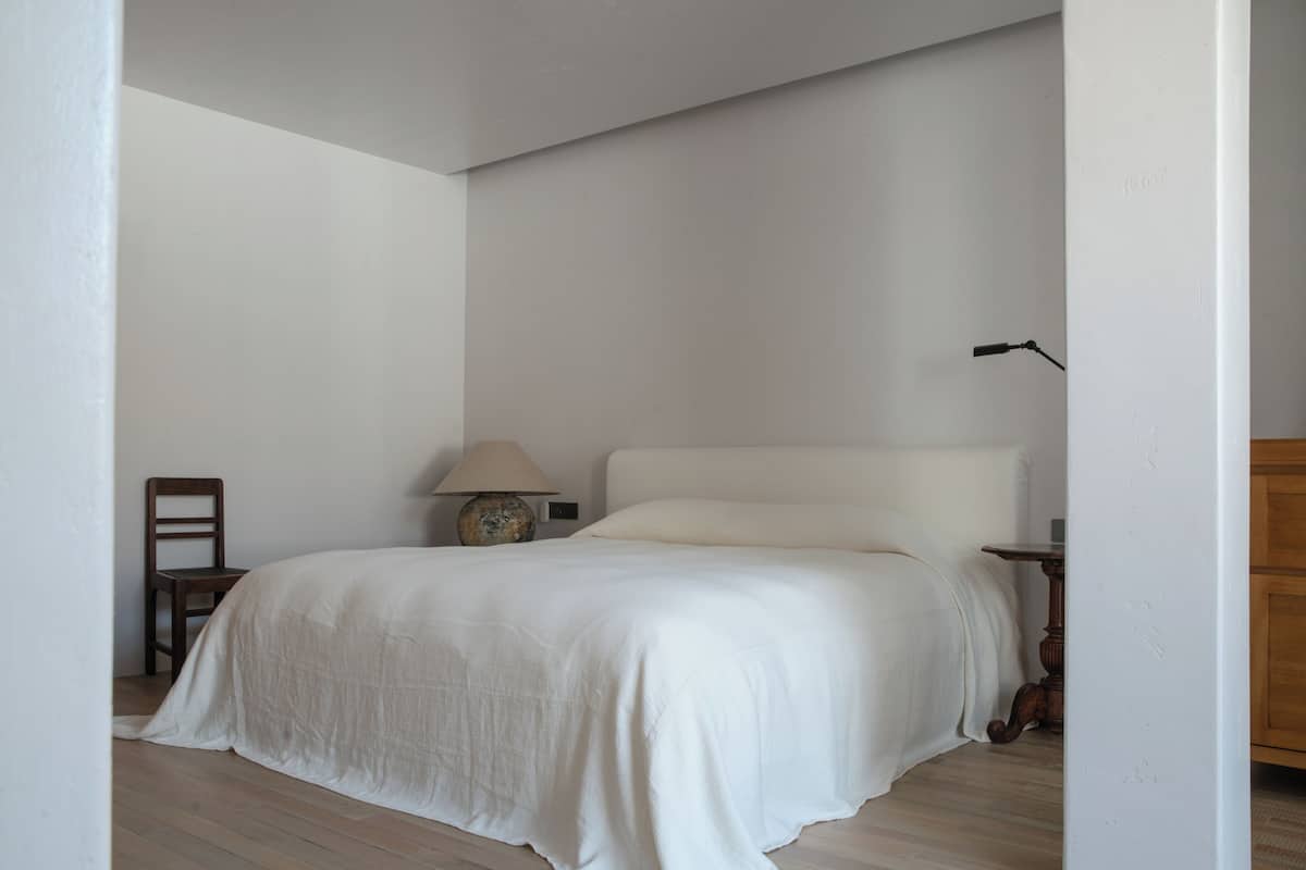 Une chambre à coucher avec un grand lit, une table de chevet avec une lampe, une chaise et une armoire en bois.