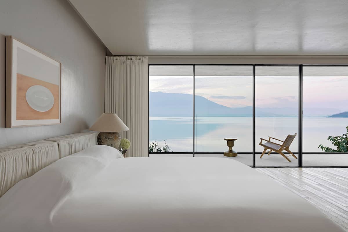 Une chambre avec un grand lit, une vue sur la mer et un fauteuil près de la fenêtre.