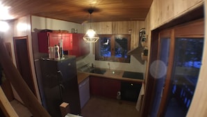 A compact kitchen with wooden cabinets, a refrigerator, a sink, and a window with a view of trees. - Chalet Ours Blanc ORS Nature & Quiet 6 Pers (Chatel)