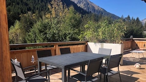 A wooden deck with a table and chairs, surrounded by a wooden fence, overlooking a forested mountain area. - Chalet Ours Blanc ORS Nature & Quiet 6 Pers (Chatel)