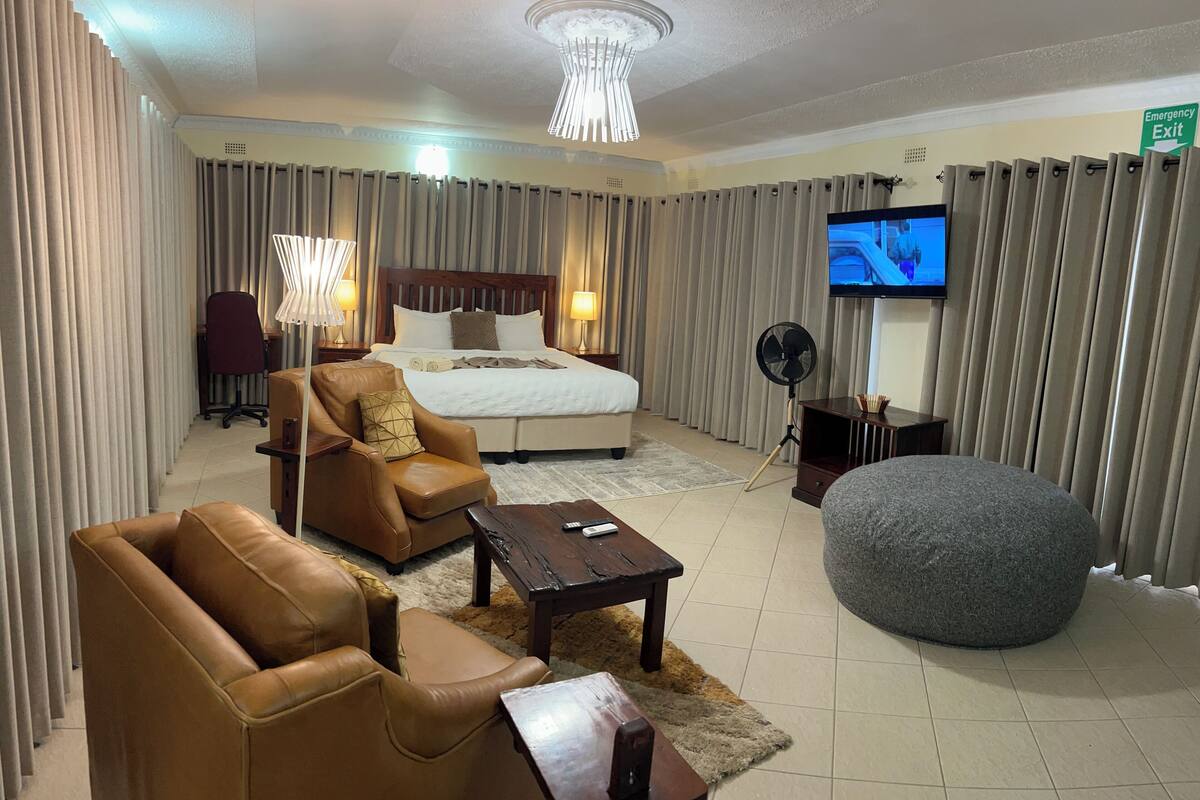 Een hotelkamer met een bed, een leren fauteuil, een poef en een televisie.