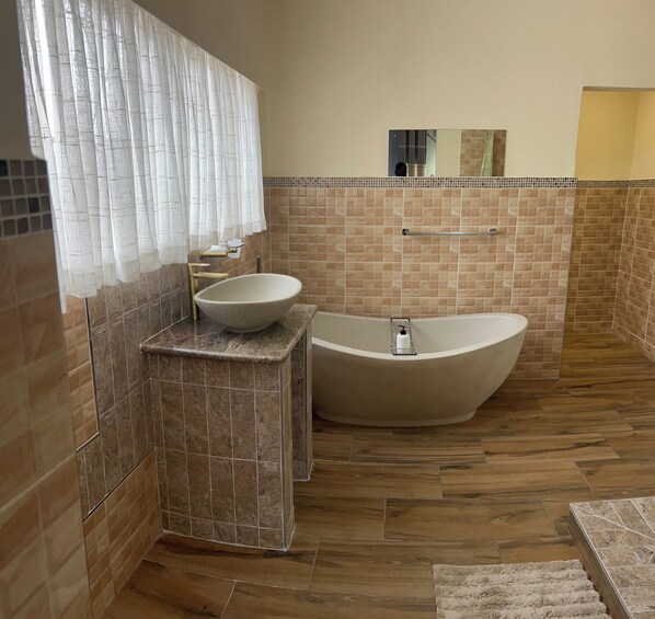 A bathroom with a freestanding bathtub, a sink with a marble countertop, and a tiled wall with a mosaic pattern. - Gunhill Avenue Guesthouse (Harare)
